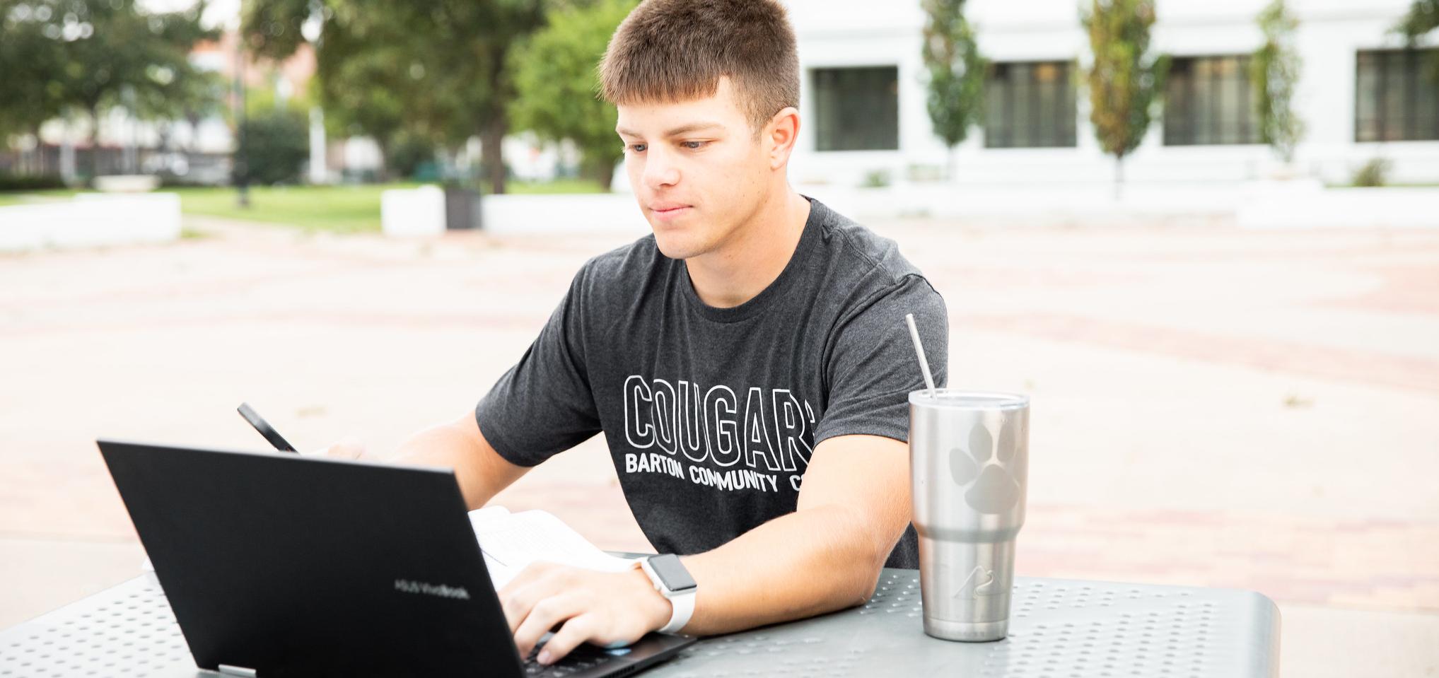 Student sitting outside at a table, with their computer and dring