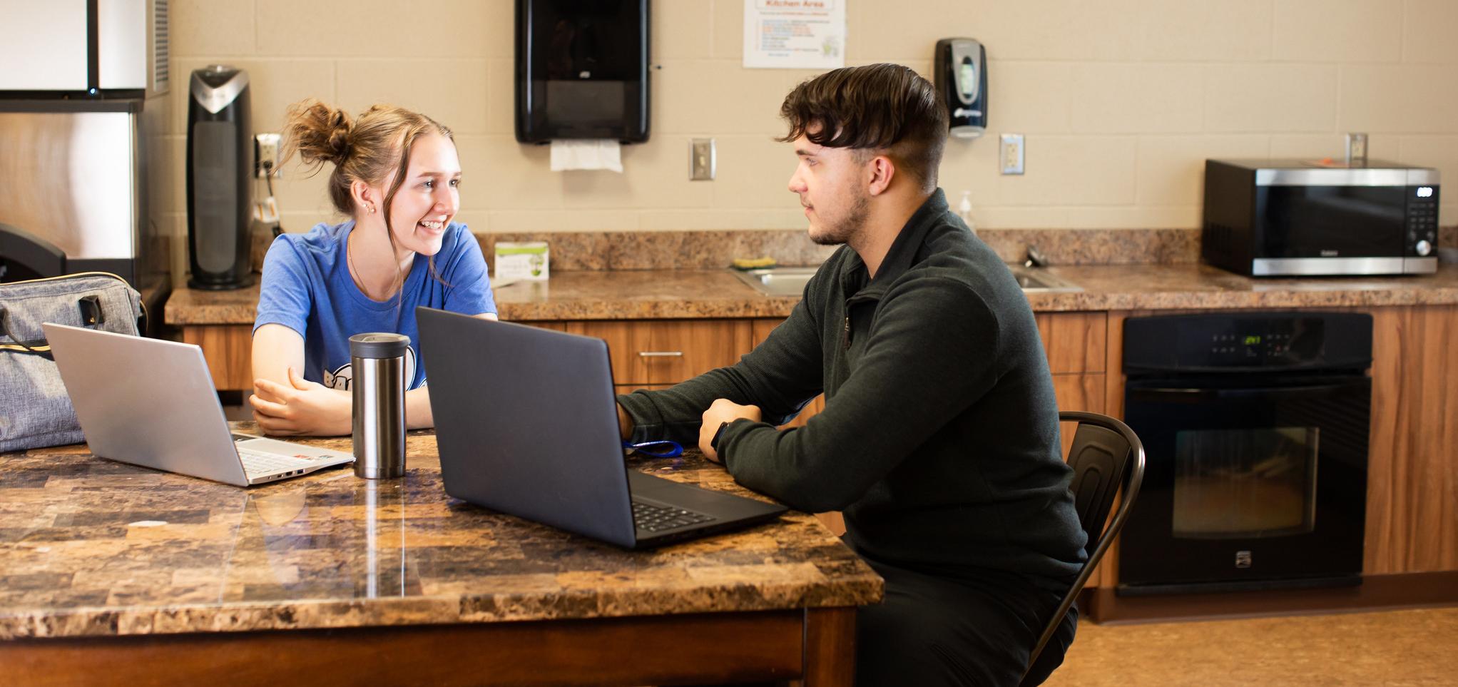 Two students sitting at a table with laptops open